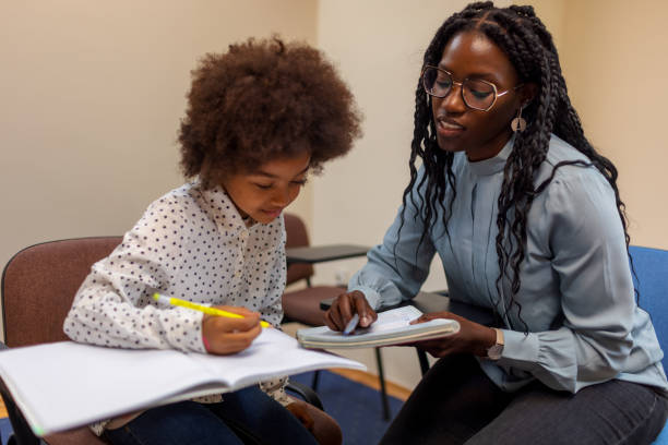 Black teacher helps her student, little girl, with reading and writing.